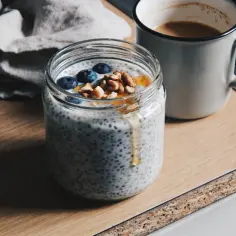 Pudding chia w słoiku z jagodami, orzechami i miodem, obok kubek kawy. Zdrowy początek dnia.