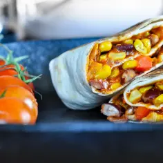 Pyszne burrito z kukurydzą, fasolą i papryką. Czy tortilla jest wegańska? Wygląda na to, że tak! Obok świeże pomidorki.