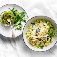 Delikatny makaron z cukinią i ziołami, idealny jako makaron z cukinia dla niemowlaka. Obok miseczka zielonego pesto.