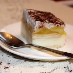 Pyszna szarlotka "Delicja" z kremem i jabłkami, posypana kakao, czeka na talerzyku z łyżeczką.
