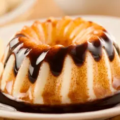 Pyszny, kremowy pudding w kształcie babeczki, polany czekoladą, z kawałkami banana obok. Co to pudding? To deser marzeń!