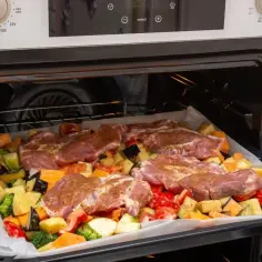 Resztki pieczonej karkówki? Zrób z nich pyszne pieczone mięso z warzywami w piekarniku. Na blasze ułożono kawałki karkówki i kolorowe warzywa.