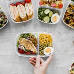 Różnorodne pojemniki z jedzeniem, od sałatek po kanapki i dania z kurczakiem, tworzą apetyczny wybór menu catering.