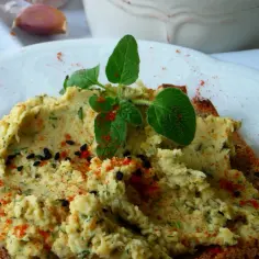 Pyszna pasta z ciecierzycy dla niemowlaka na grzance, posypana papryką i czarnuszką, ozdobiona świeżymi ziołami.