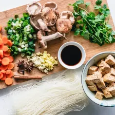Składniki na szybki obiad z tofu: pokrojona marchewka, dymka, grzyby shiitake, czosnek, imbir, sos sojowy, kolendra, ryżowy makaron i kostki tofu.
