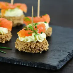 Eleganckie przekąski z łososiem i kremem na ciemnym kamieniu. Idealny sposób, jak serwować przystawki na przyjęciu.