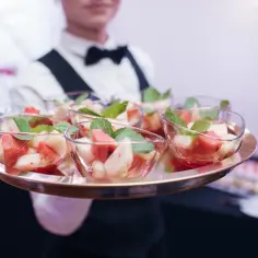Taca z deserami owocowymi w szklanych pucharkach, podawana przez kelnera.