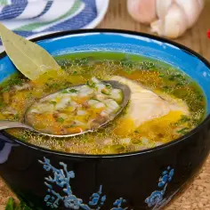 Aromaticzna zupa z kaszą gryczaną, kawałkiem kurczaka i warzywami, podana w czarnej misce z niebieskim rantem. Na łyżce widać bogactwo składników.