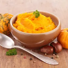 Miseczka z pomarańczowym puree z dyni, obok małe dynie i kasztany. Idealne na jesienne dni, gdy chcesz wiedzieć, jak zrobić puree z dyni.
