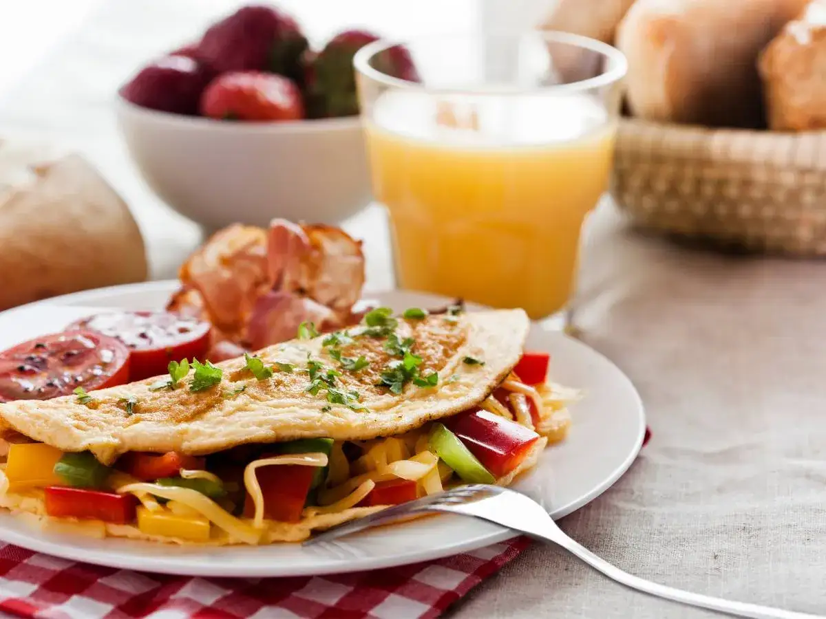 Pyszny omlet z warzywami i bekonem, idealny pomysł na śniadanie bez chleba. Obok szklanka soku i miseczka truskawek.