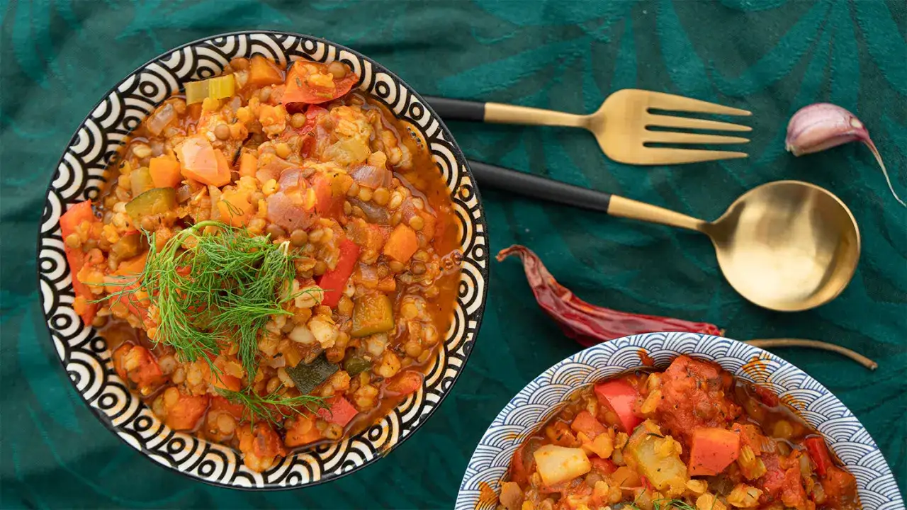 Gęsty, aromatyczny gulasz z soczewicy z warzywami, udekorowany koperkiem. Obok złote sztućce i suszona papryczka chili.