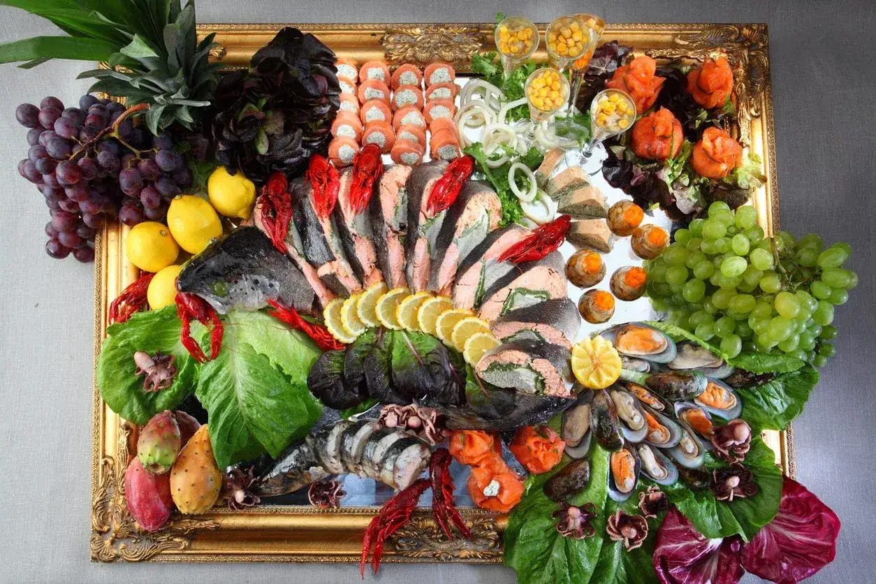 Bogaty wybór menu catering: ryby, owoce morza, owoce, warzywa i przystawki na złotej tacy.