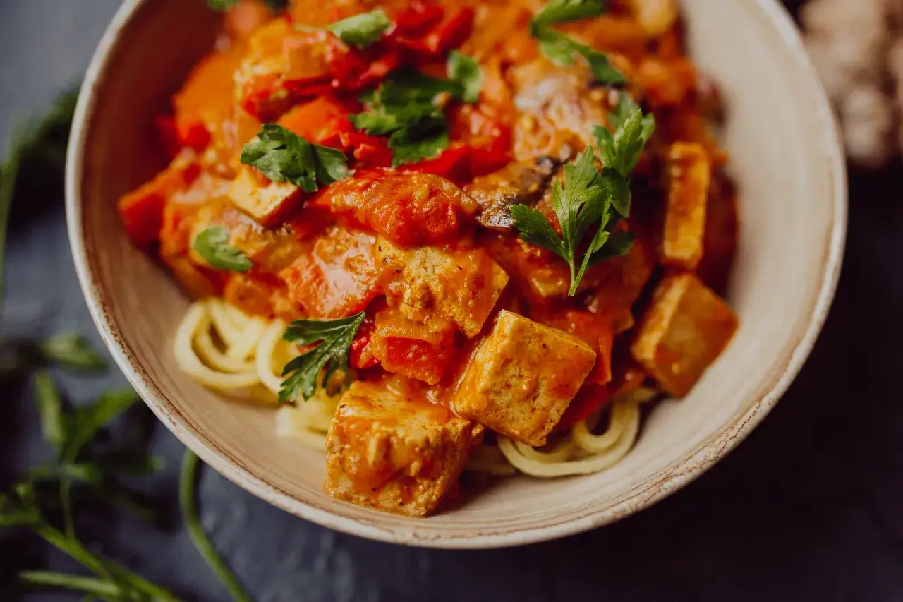 Tofu w sosie pomidorowym z makaronem, udekorowane natką pietruszki. Pyszne i zdrowe danie.