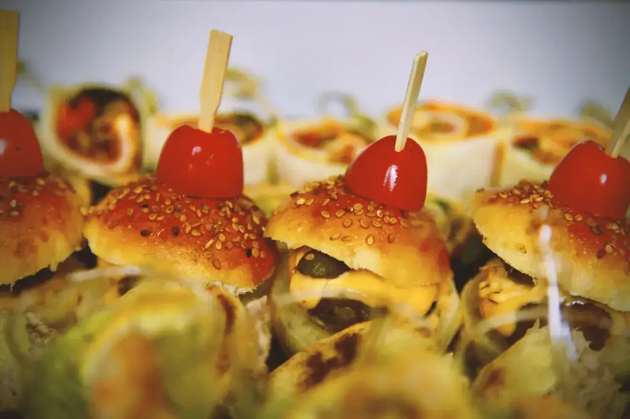 Mini burgery z pomidorkiem i sezamem, ułożone na talerzu, tworzą apetyczną przekąskę.