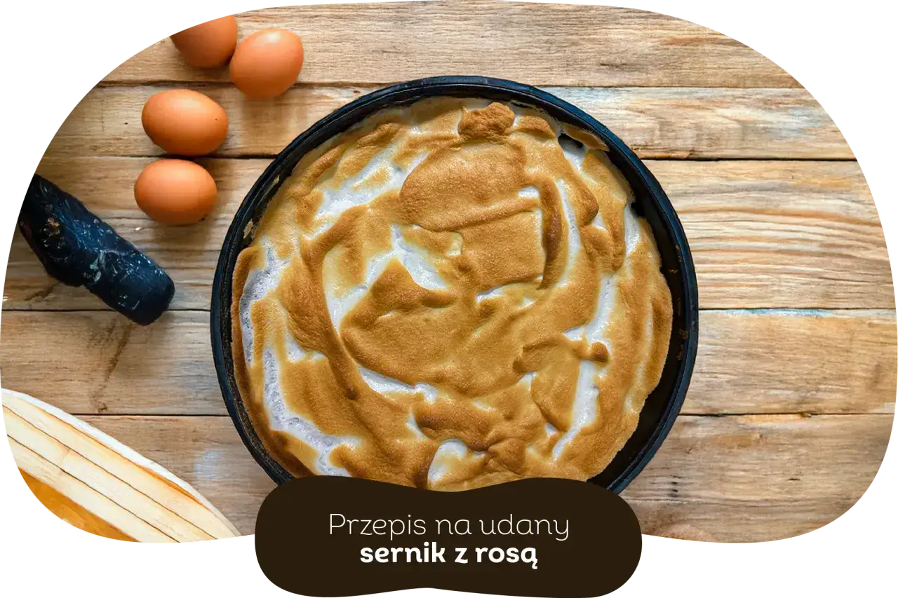 Sernik z pianką na drewnianym tle. Kilka jajek obok. Dowiedz się, dlaczego nie wychodzi rosa na serniku i jak zrobić idealny deser.