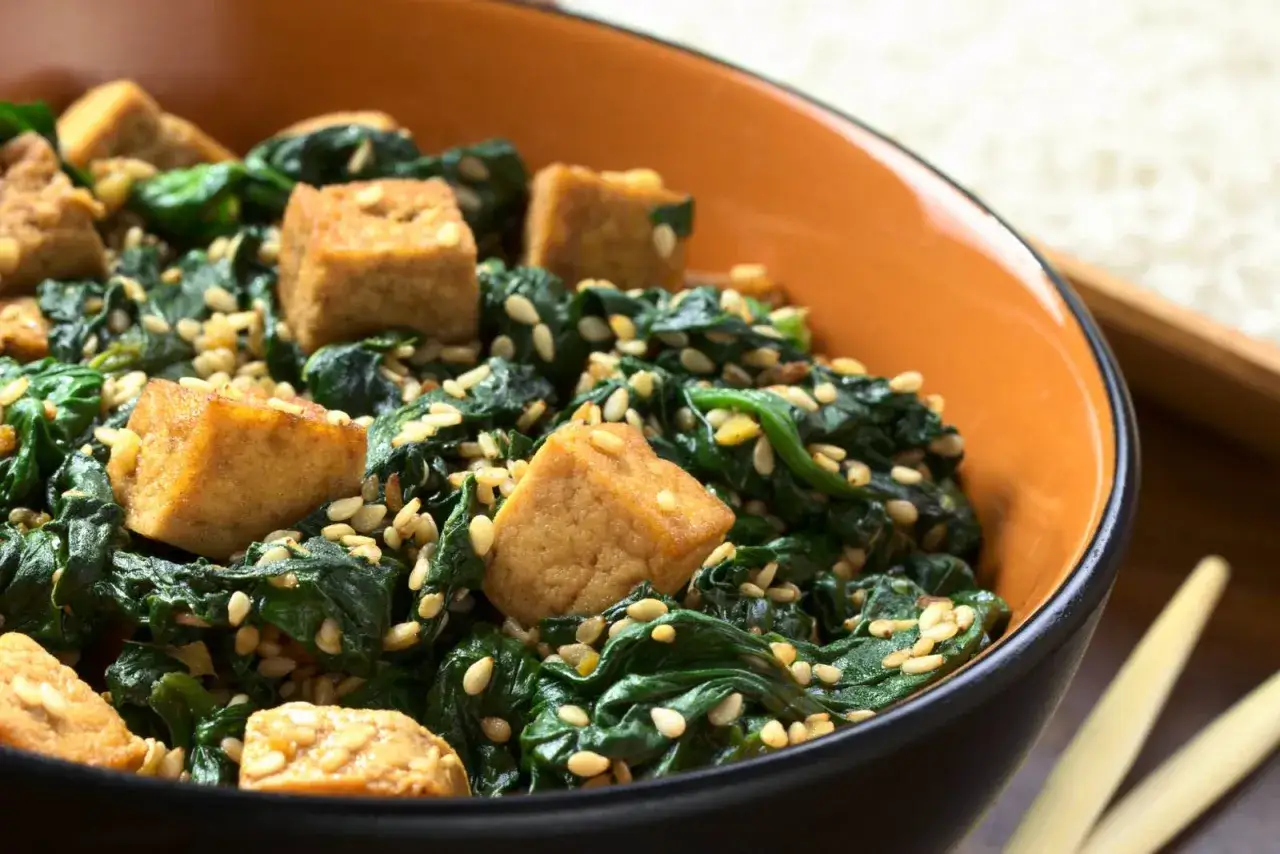 Tofu na śniadanie z duszonym szpinakiem i sezamem. Pyszne i zdrowe danie w pomarańczowej misce.