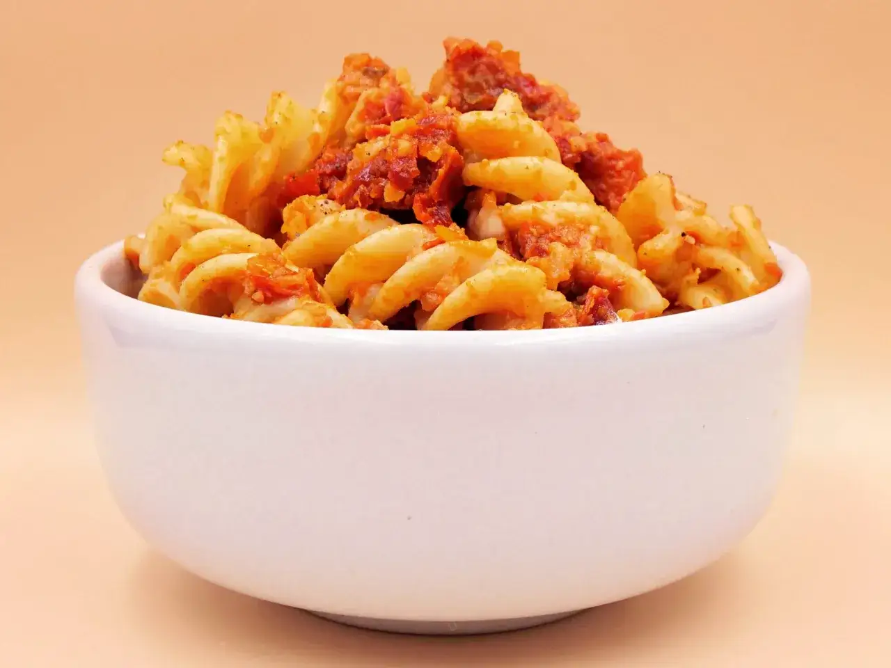 Fusilli z aromatycznym pesto i kawałkami suszonych pomidorów w białej miseczce.