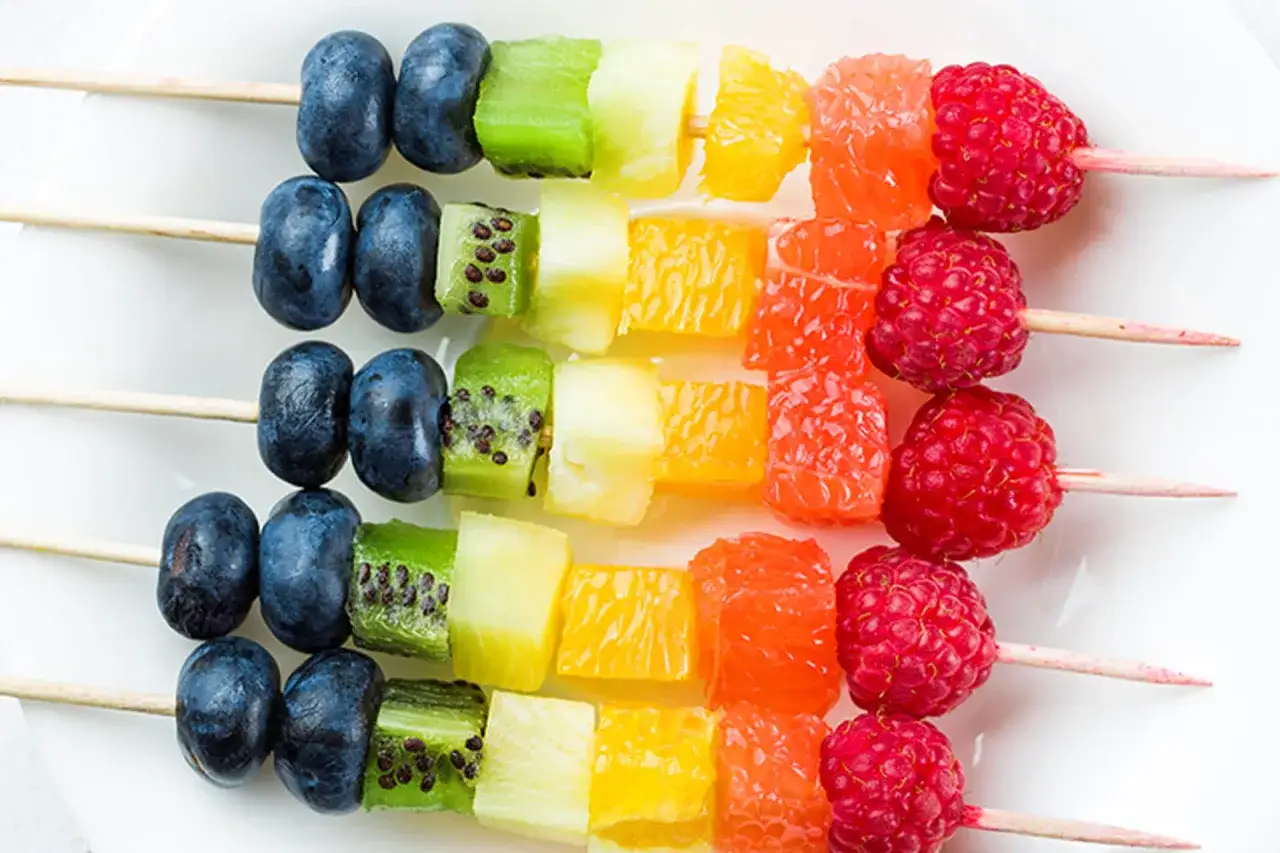 Kolorowe szaszłyki owocowe: borówki, kiwi, ananas, pomarańcza, grejpfrut i maliny. Idealny sposób, jak efektownie podać owoce na talerzu.