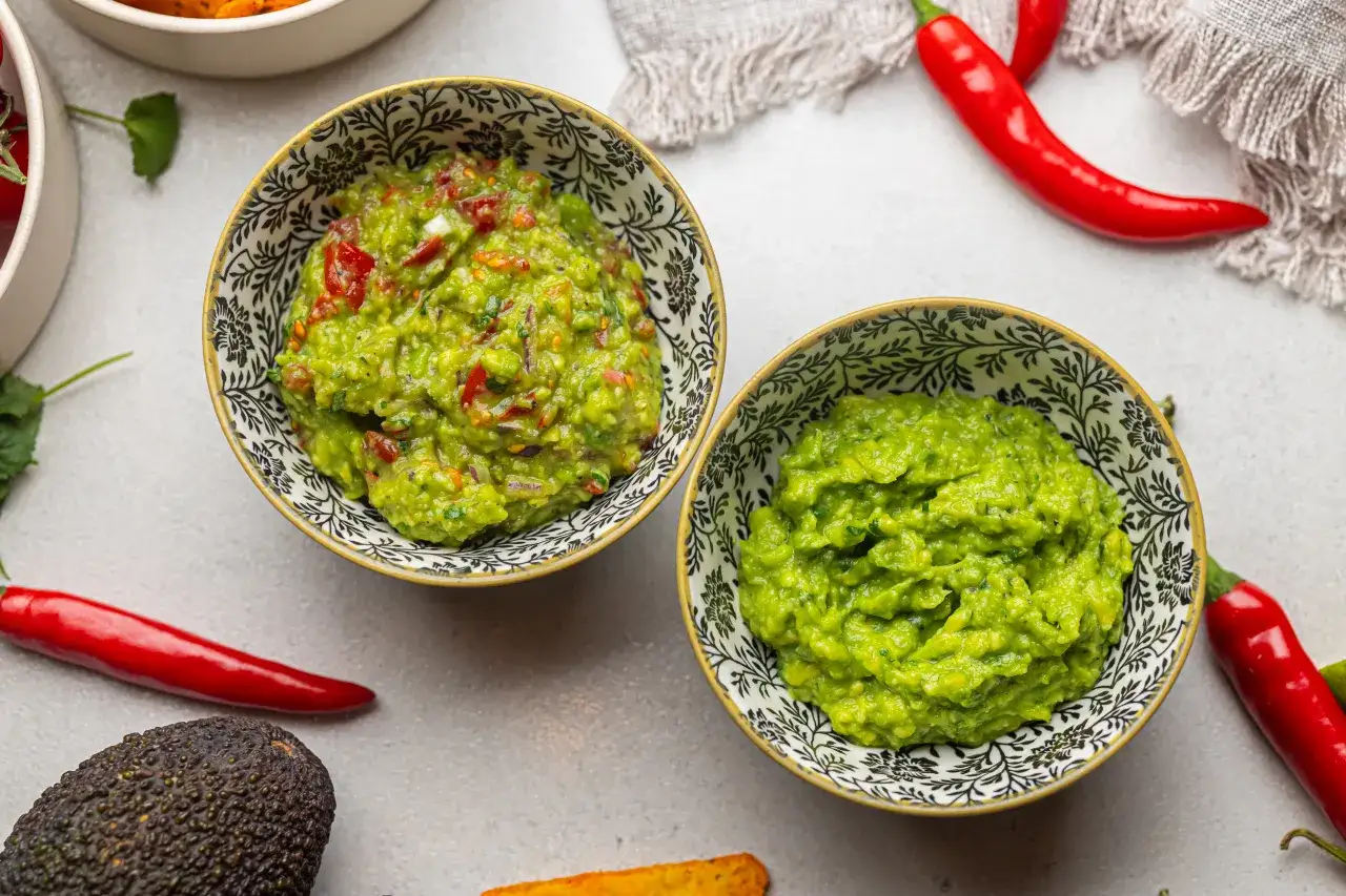 Dwie miseczki z guacamole, idealne do nachosów, tortilli lub jako dodatek do dań. Obok awokado i papryczki chili.