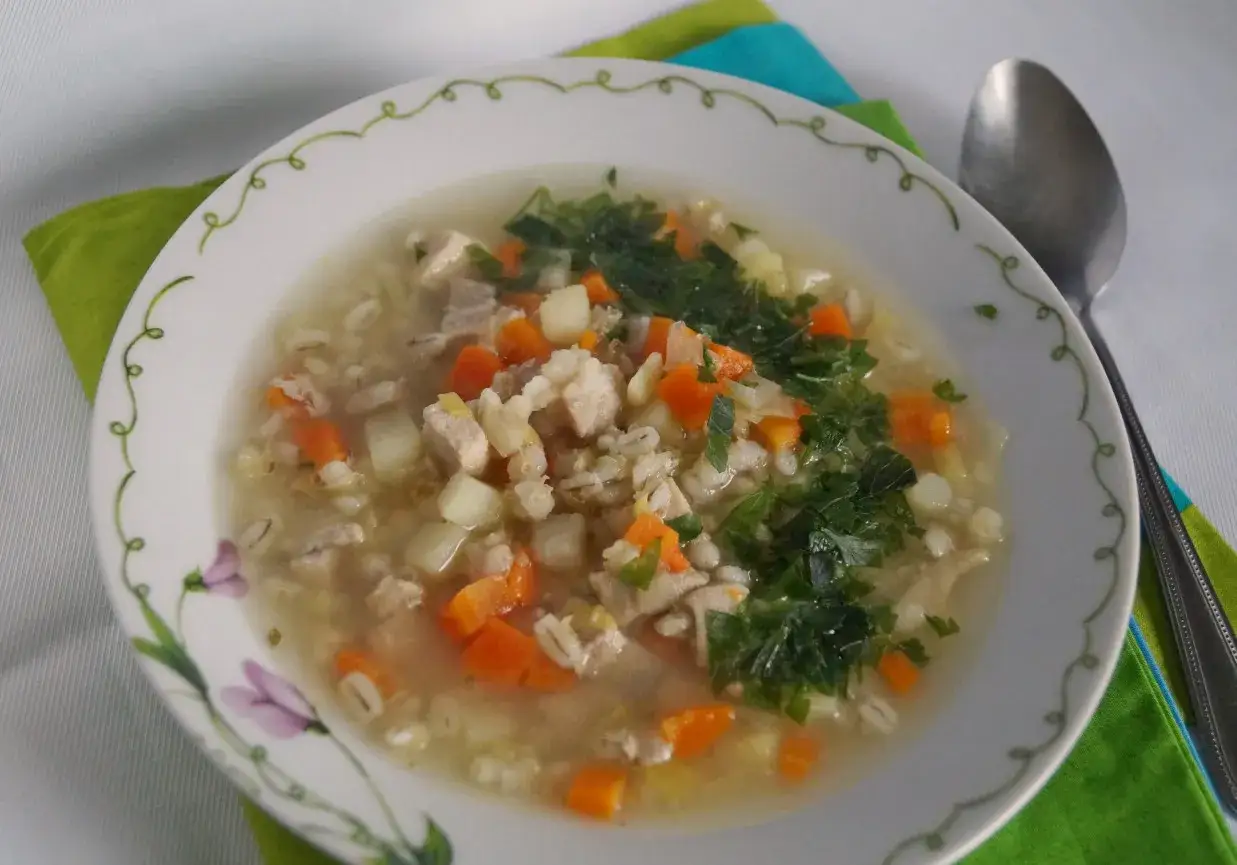 Syci krupnik z kaszą pęczak, kawałkami kurczaka, marchewką i ziemniakami, posypany natką pietruszki.