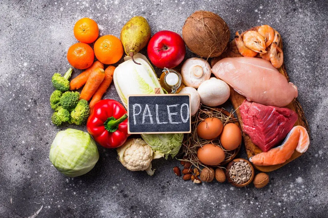 Na stole leżą produkty do diety paleo: mięso, ryby, jajka, warzywa, owoce, orzechy i nasiona.