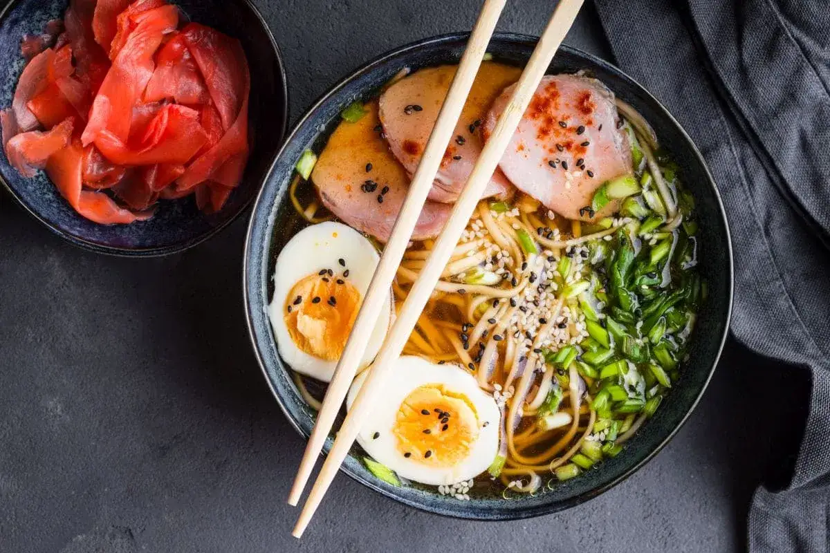 Pyszna zupa ramen z jajkiem, mięsem i szczypiorkiem. Idealna odpowiedź na pytanie, jaką zupę na obiad. Obok miseczka marynowanego imbiru.