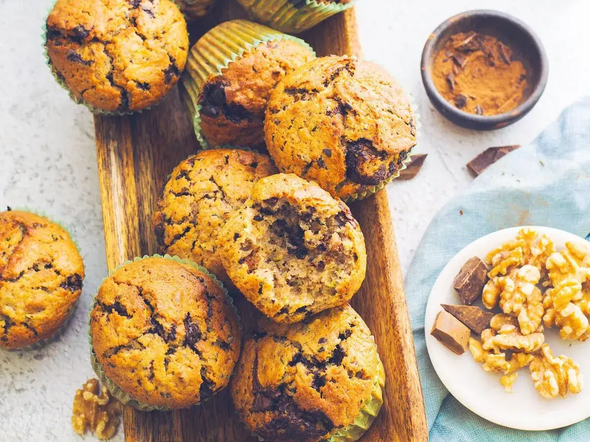Pyszne muffinki z cukinią i kawałkami czekolady, obok orzechy włoskie i czekolada. Idealne na podwieczorek!