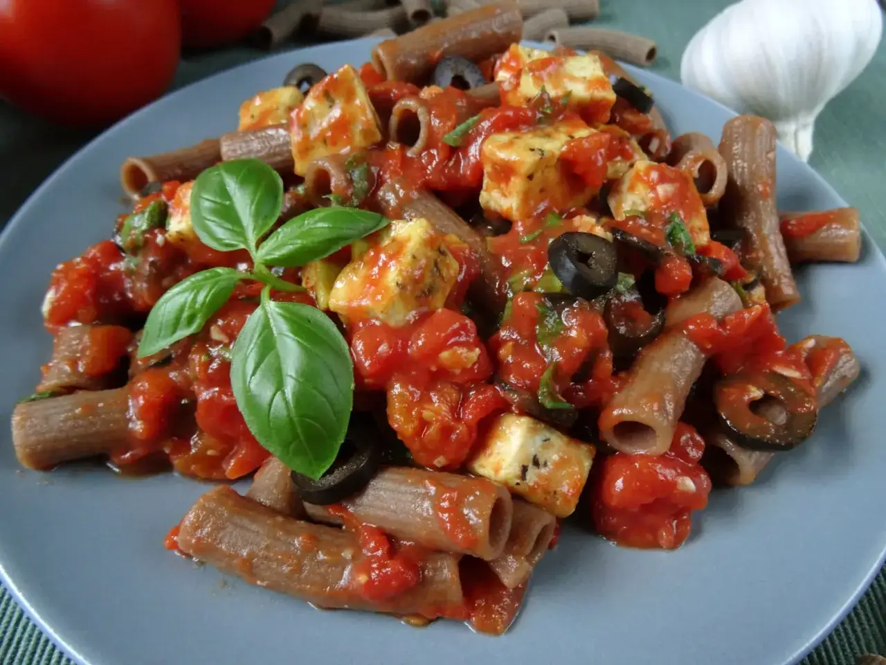 Tofu w sosie pomidorowym z makaronem pełnoziarnistym, oliwkami i świeżą bazylią. Pyszne i zdrowe danie.