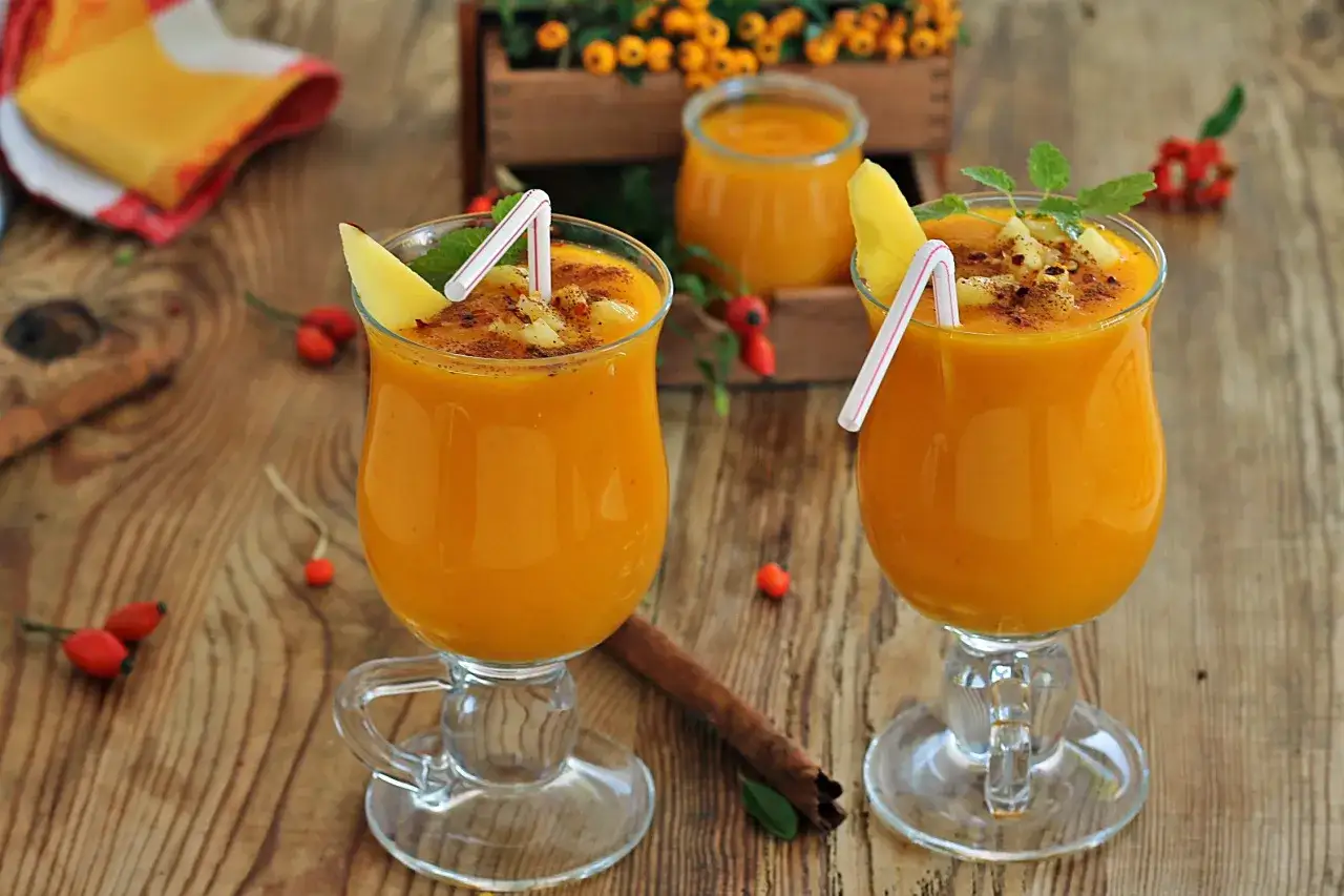 Dwa pyszne koktajle z dyni, udekorowane plasterkiem mango i listkiem mięty, na drewnianym stole.