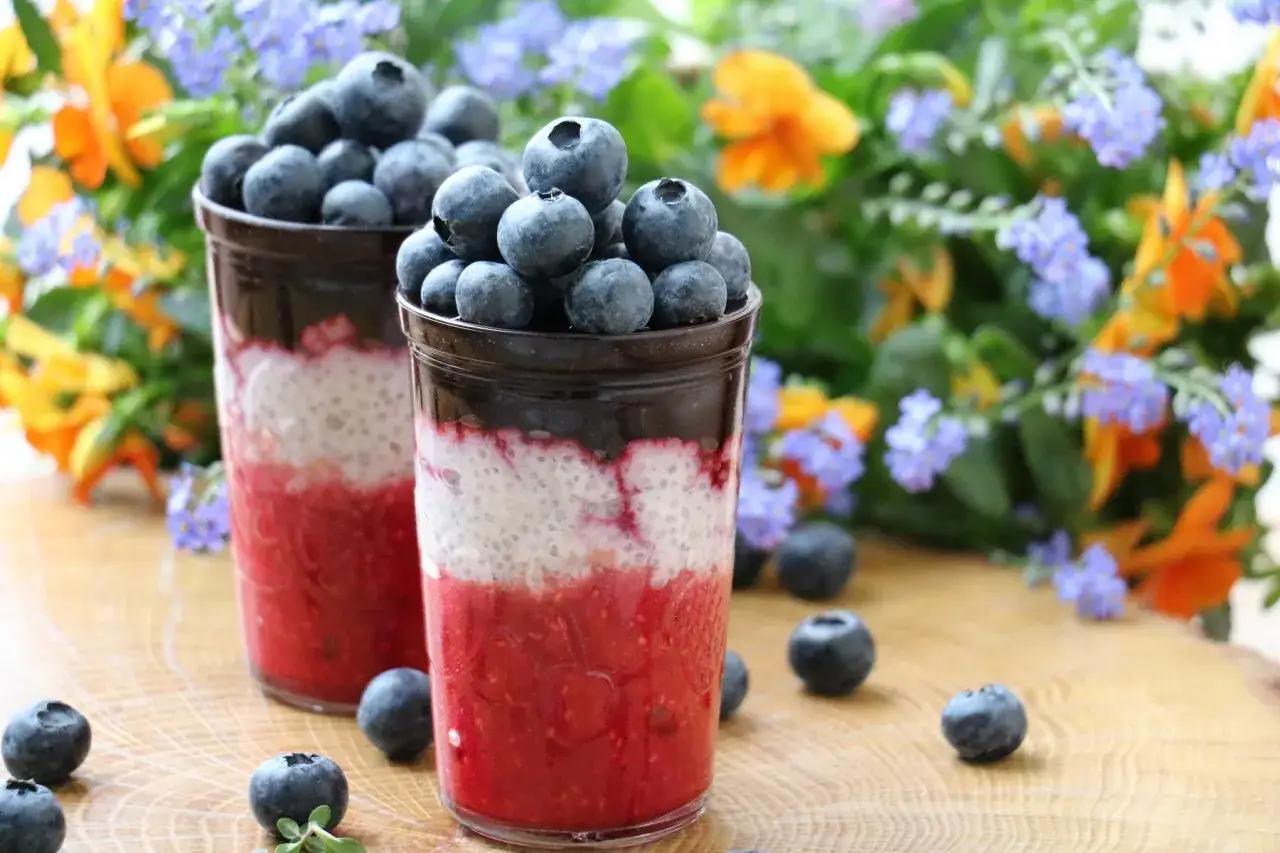 Pyszny pudding chia z malinami i borówkami, udekorowany świeżymi owocami i kwiatami.